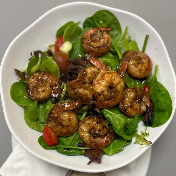 A white bowl filled with a fresh green salad topped with grilled shrimp and cherry tomatoes.