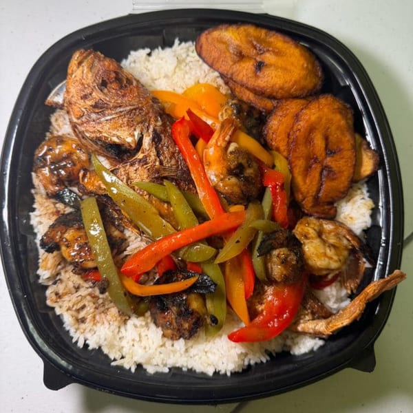 Jamaican dish with whole fried fish, shrimp, bell peppers, plantains, and rice in a black container.