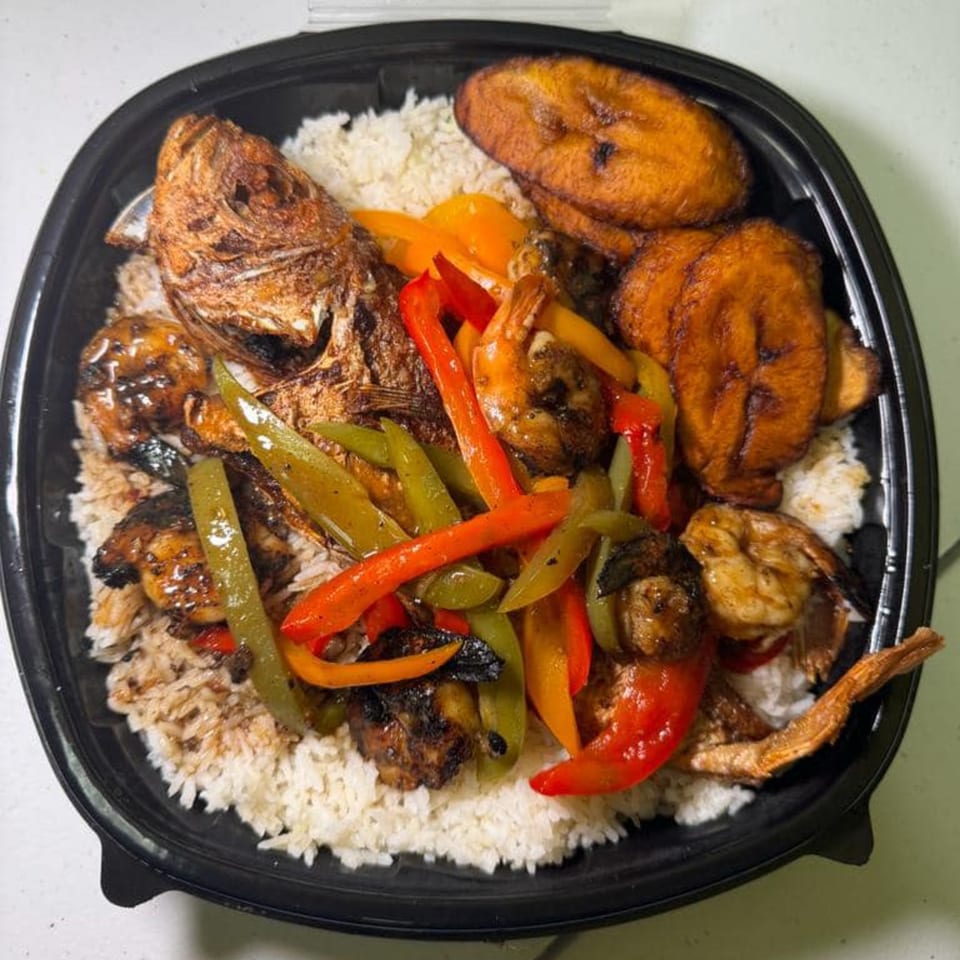 Jamaican dish with whole fried fish, shrimp, bell peppers, plantains, and rice in a black container.